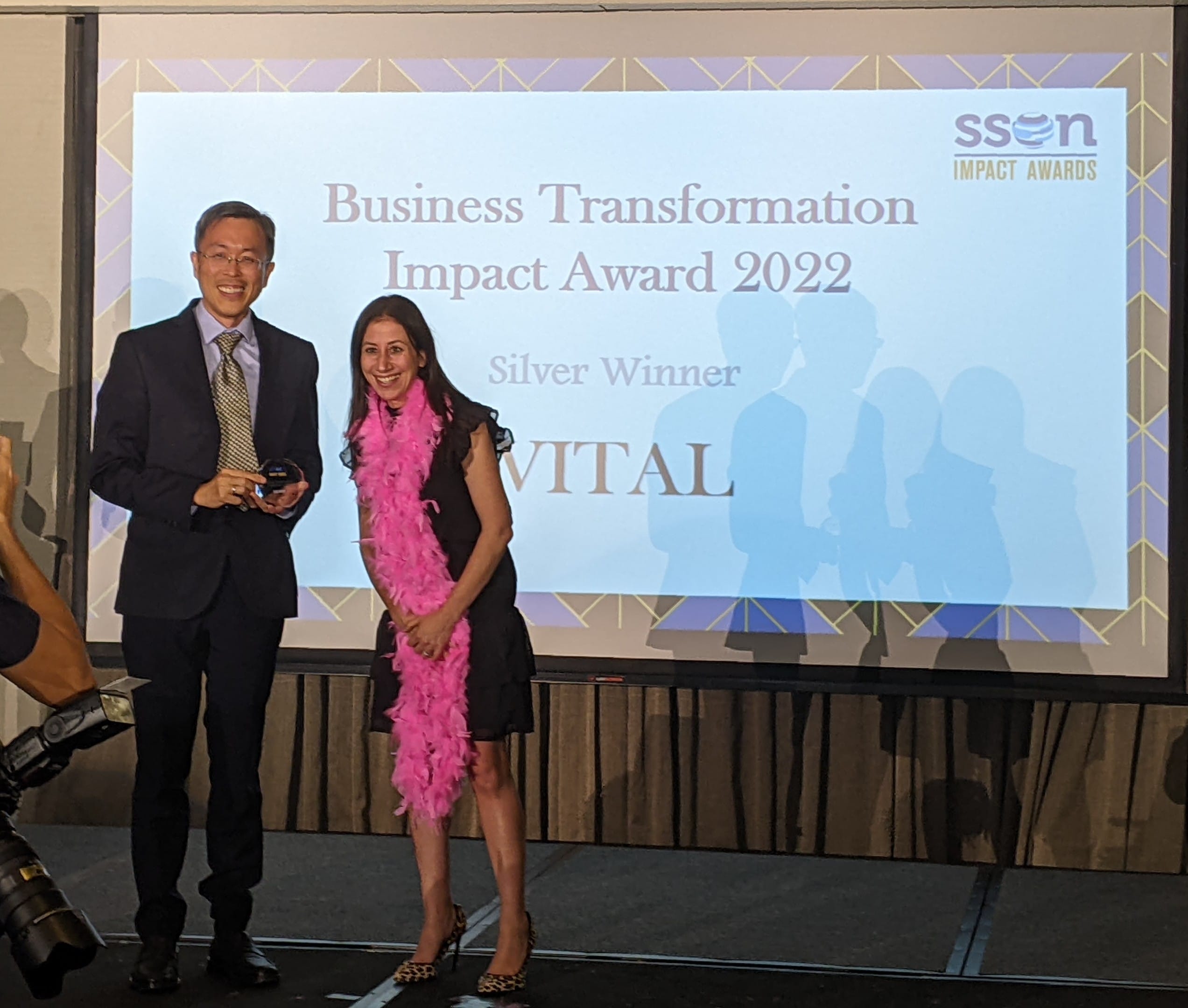 Two people stand on stage before a screen reading SSON Business Transformation Impact Award 2022 Silver Winner VITAL.
